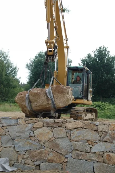 Bagger setzt einen großen Stein auf eine Natursteinmauer