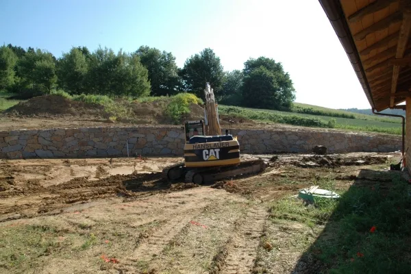 Hanslauer-Bagger vor einer langen Natursteinmauer