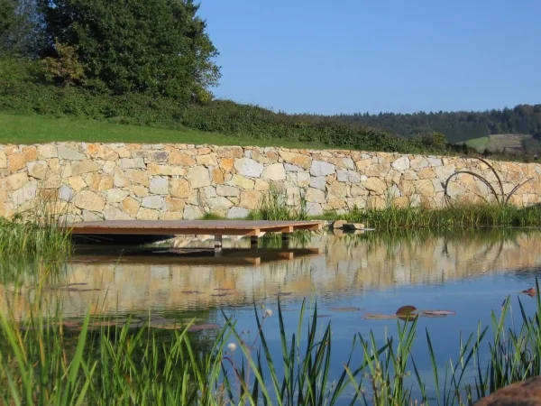 Steg über einem Teich vor einer Natursteinmauer